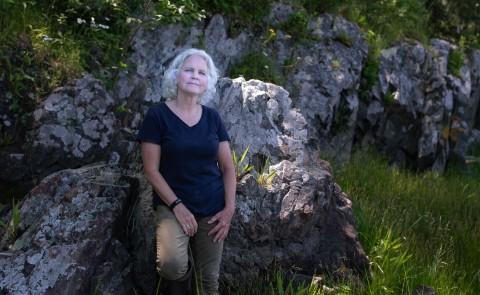 Portrait of Pam Morgan leaning up against a boulder in the woods